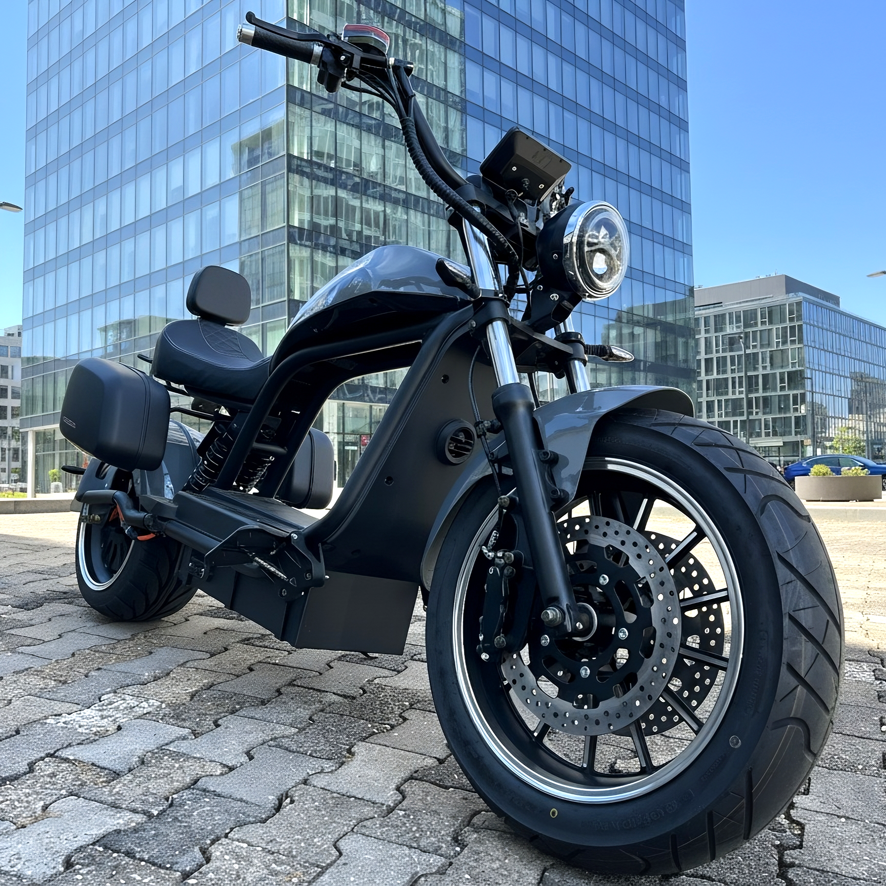 Star-Biker Chopper 6.0S E-Chopper mit Gepäcksystem vor modernem Glas-Business-Gebäude, tiefschwarzes Design, breite Reifen und stilvolle Seitenkoffer, fotografiert im urbanen Umfeld.